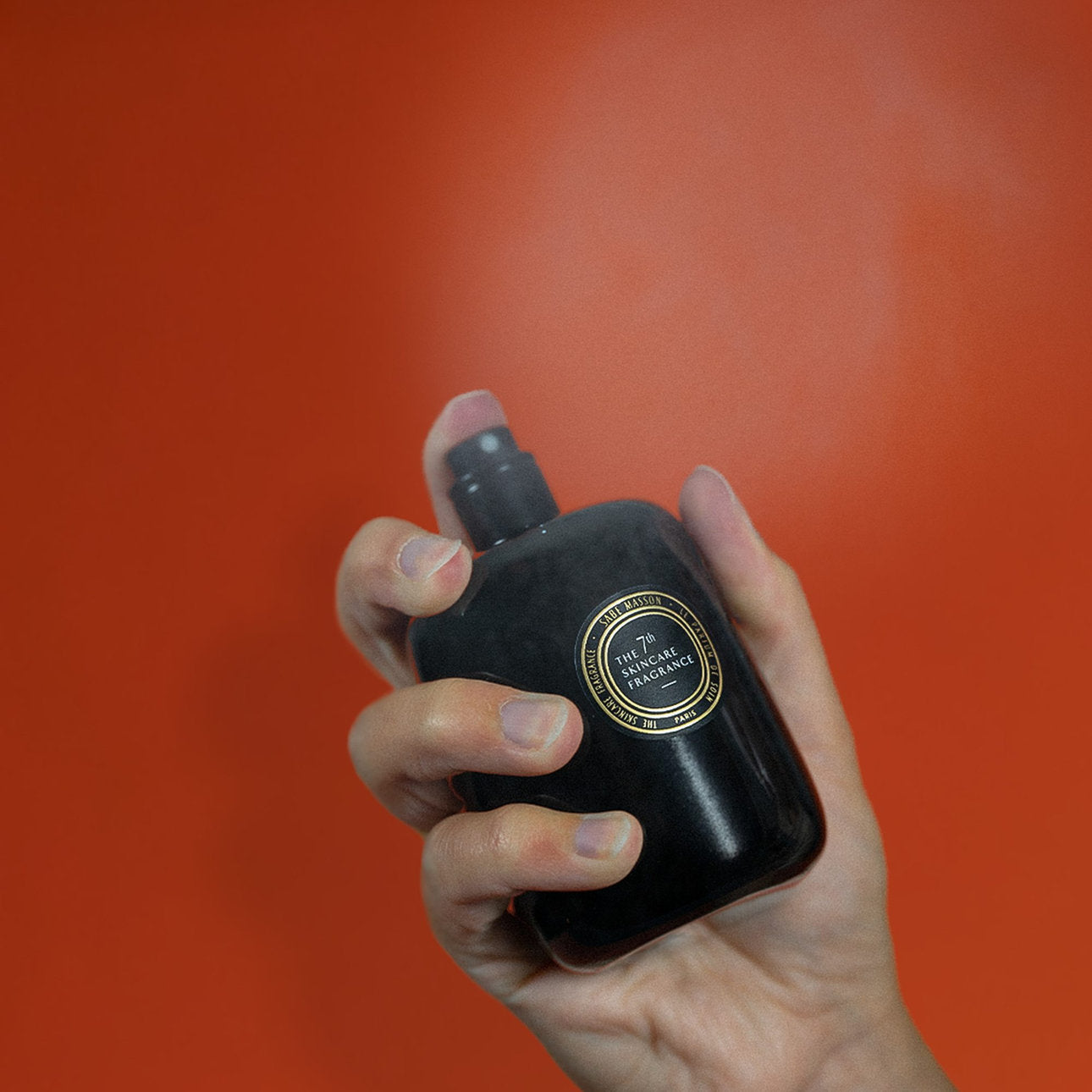 Hand hält schwarzen Parfumflakon vor rotem Grund