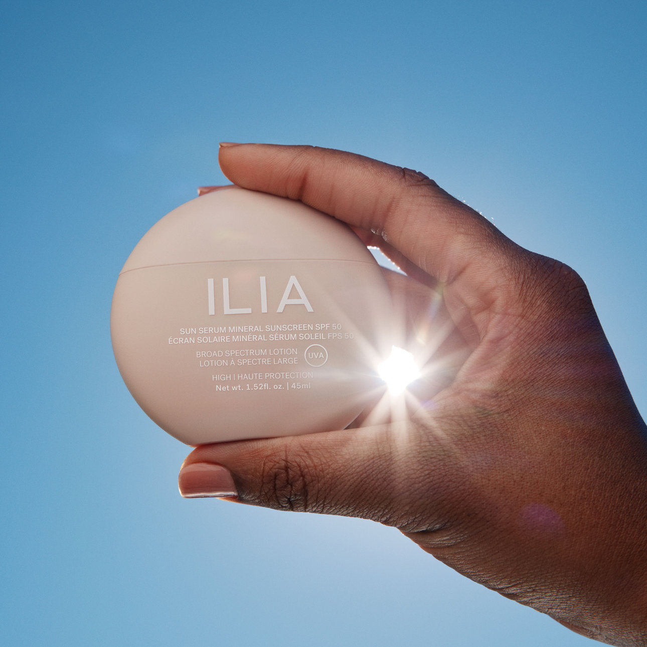Hand hält ILIA Sun Serum gegen die Sonne vor blauem Himmel – Kollektion Sonnenschutz & Pflege bei Curantus Naturkosmetik Münster