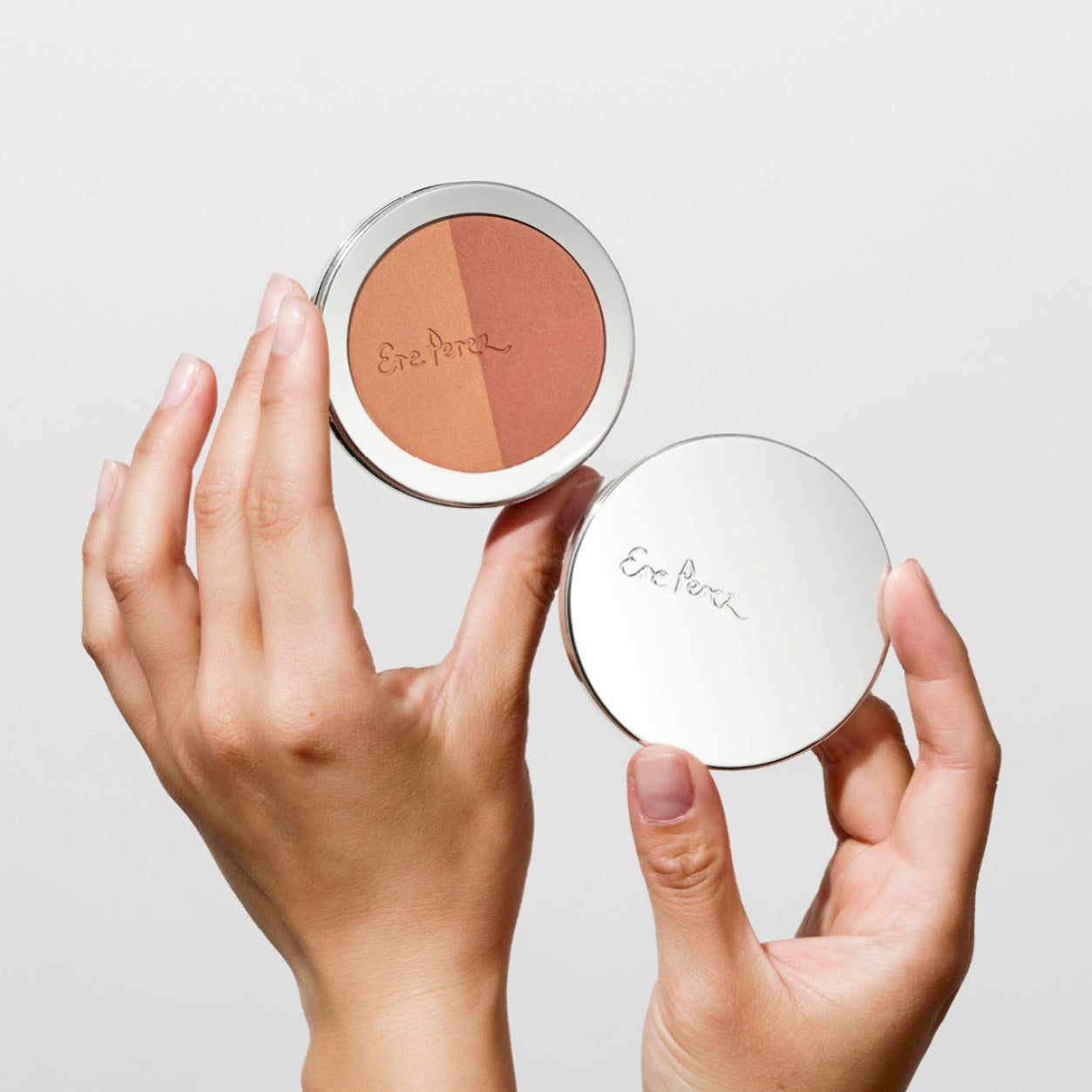 Zwei Hände halten den geöffneten Ere Perez Rice Powder Bronzer Tulum und den verspiegelten Deckel