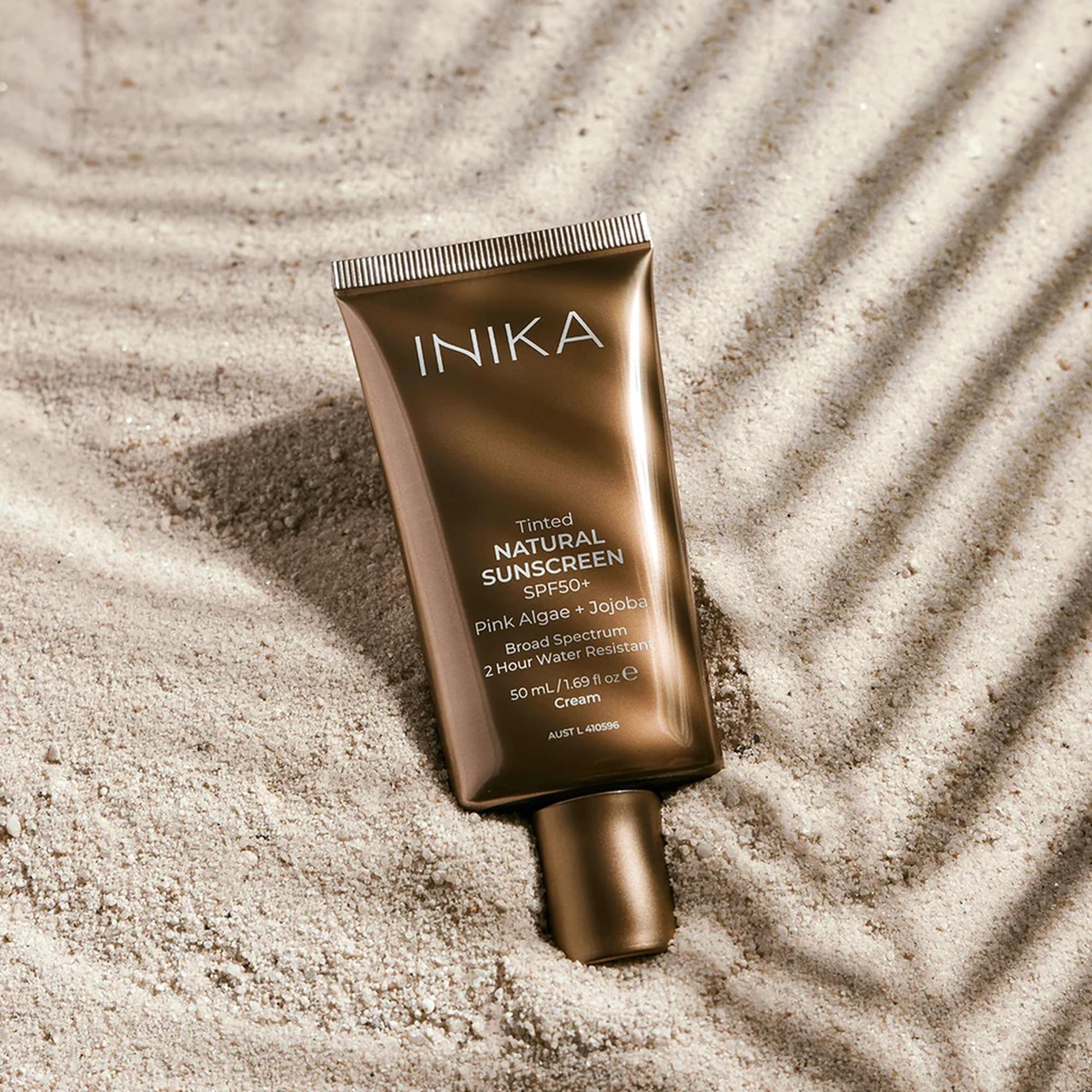 INIKA Organic Tinted Natural Sunscreen SPF50+ – Tube im Sand mit Palmenschatten