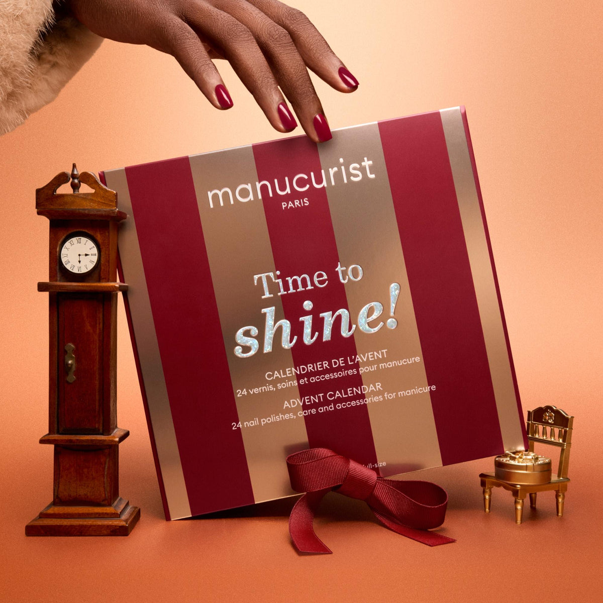 Manucurist Adventskalender 2026 Time to Shine! – Hand mit roten Nägeln auf der Box