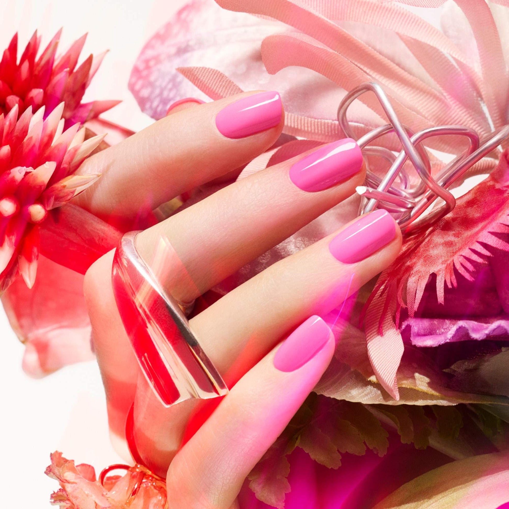 Manucurist Bloom – Hand mit pink lackierten Nägeln zwischen Blüten