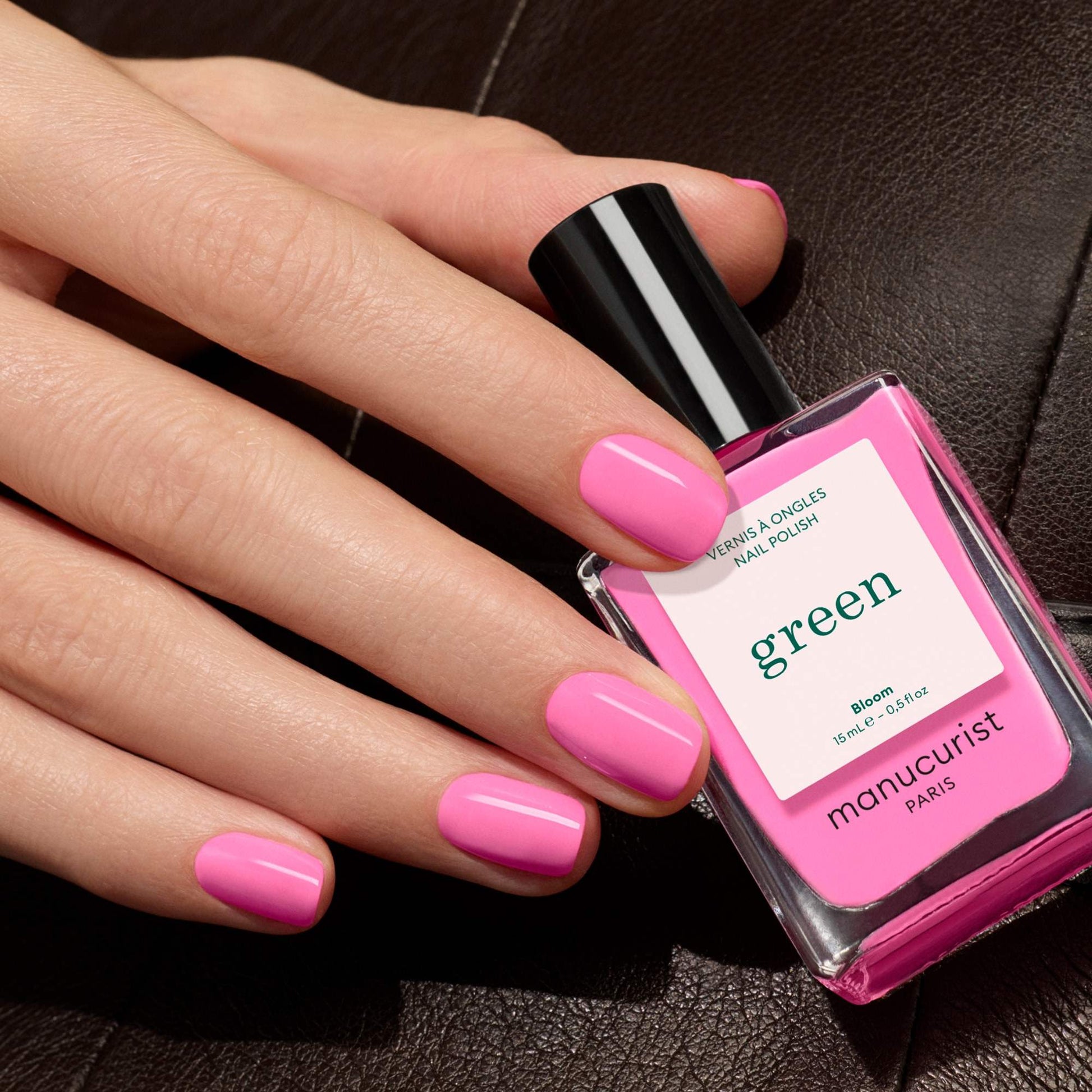 Manucurist Bloom – pinke Nägel halten den Flakon auf dunklem Leder