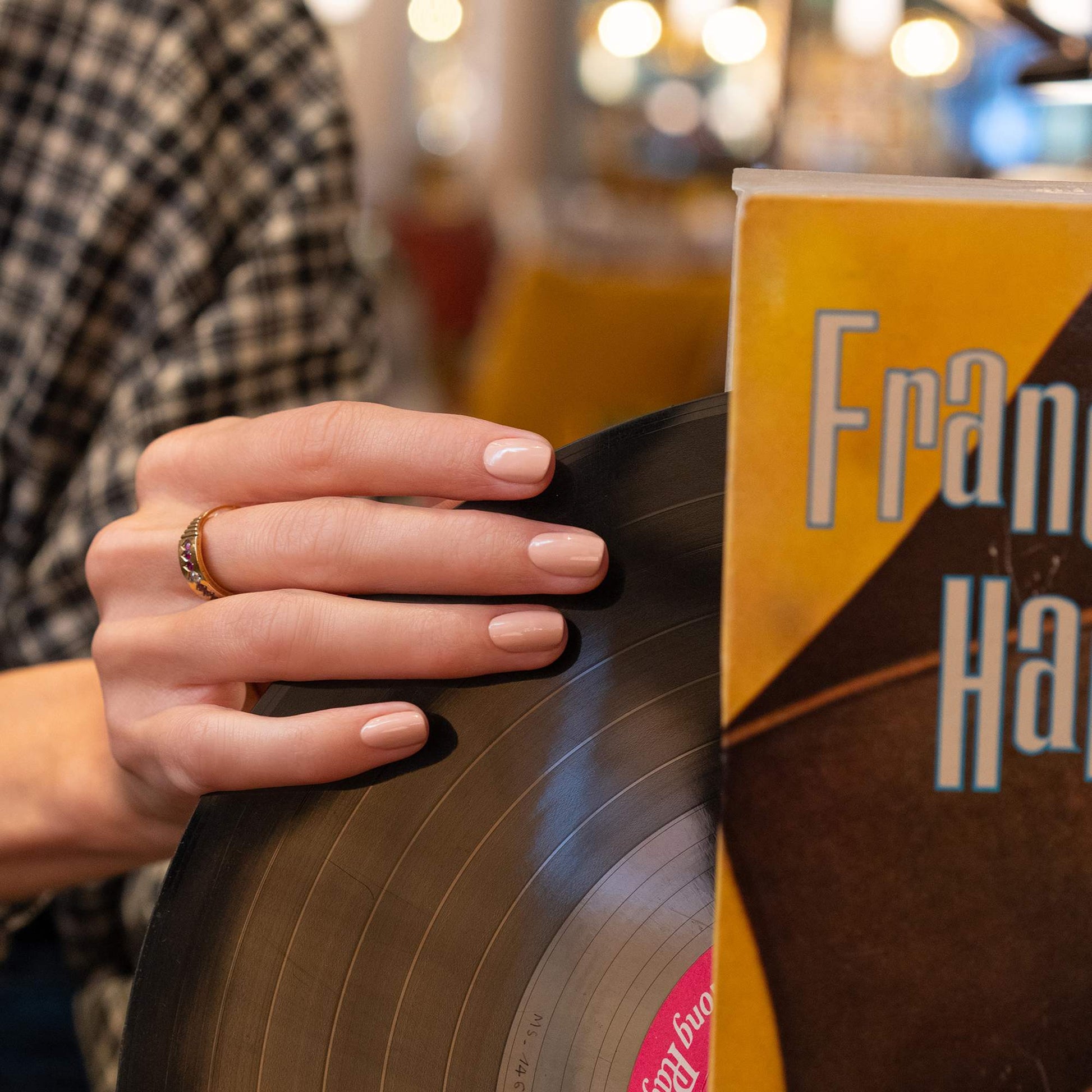 Manucurist Dune – Hand mit nude lackierten Nägeln an einer Vinylplatte