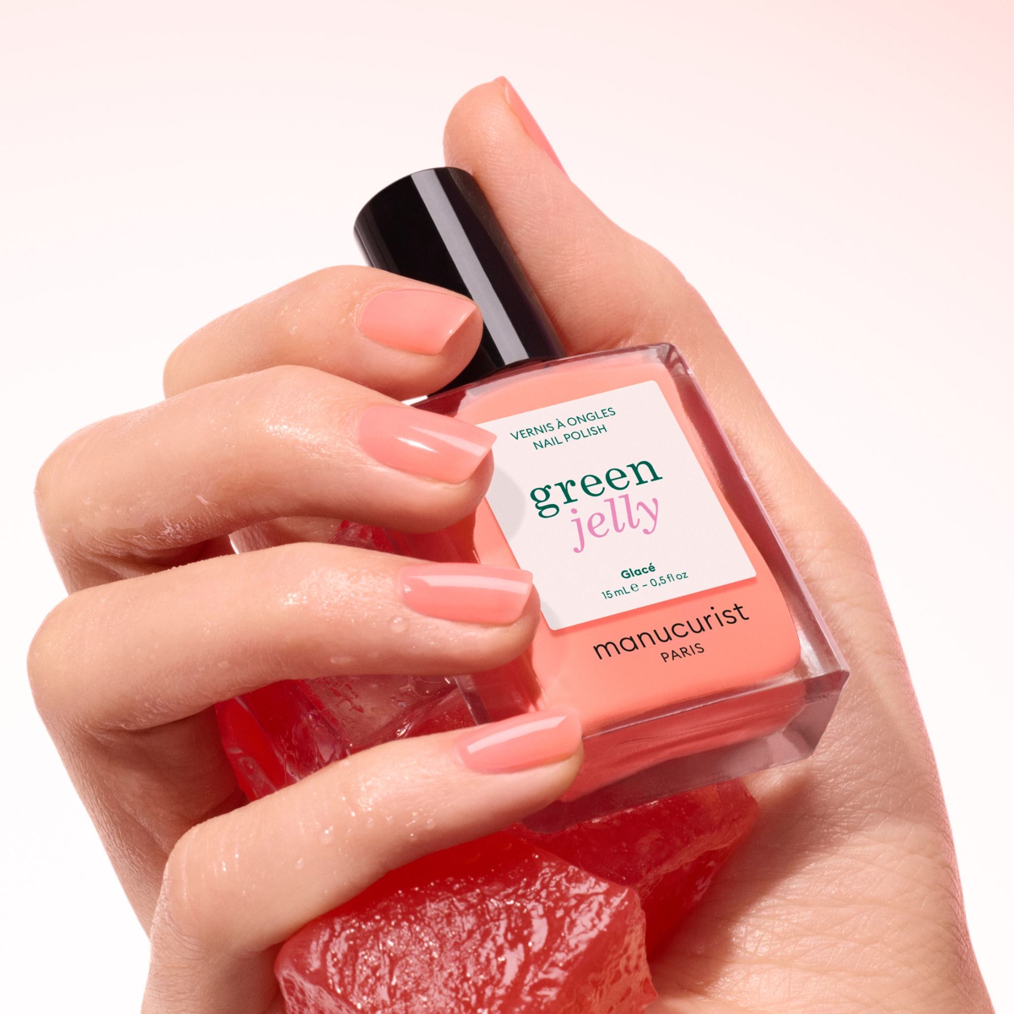 Manucurist Glacé Jelly – Hand hält den Flakon über korallroten Bonbons