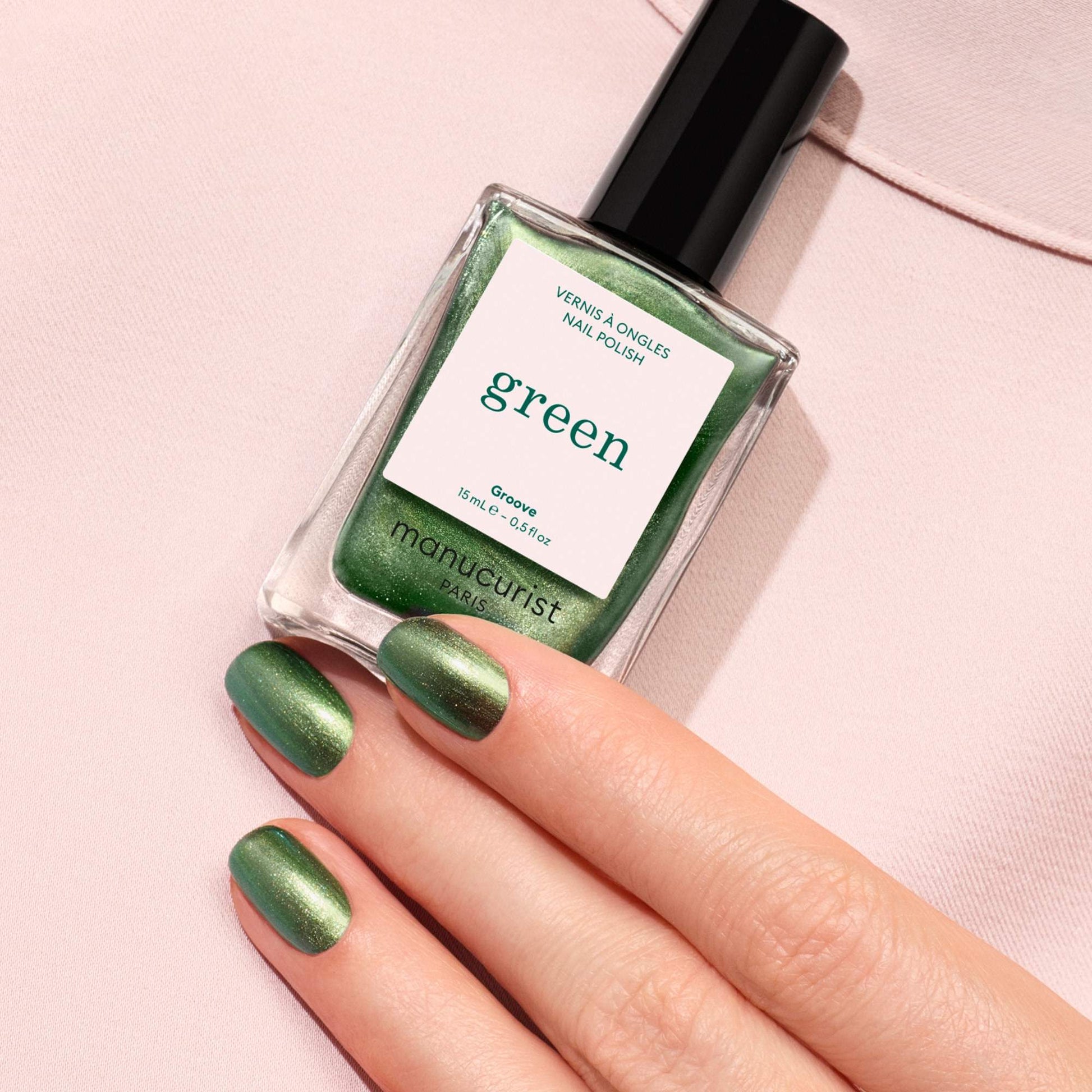 Manucurist Groove – grüne Nägel halten den Flakon auf rosa Untergrund
