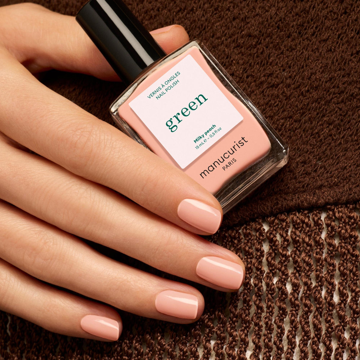 Manucurist Milky Peach – Hand mit lackierten Nägeln hält den Flakon