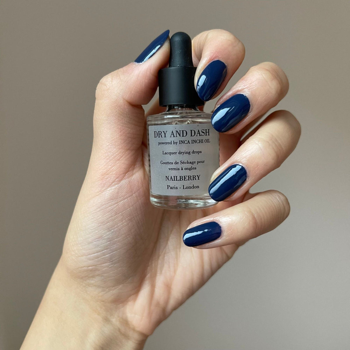 Nailberry Dry & Dash Lacquer Drying Drops, 11ml – Flasche in der Hand mit blau lackierten Nägeln