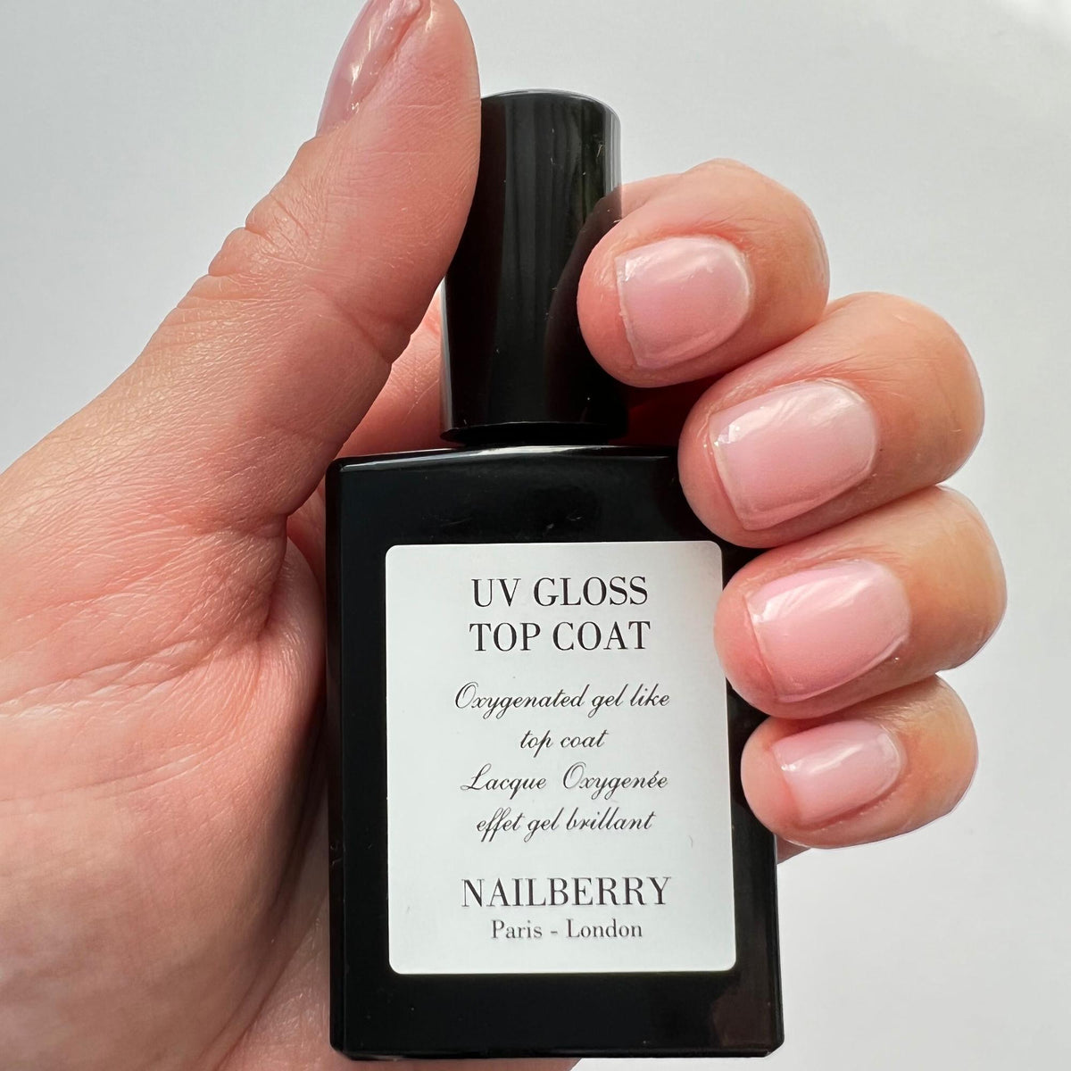 Nailberry UV Gloss Top Coat, 14ml – Flasche in der Hand mit glänzenden Nägeln