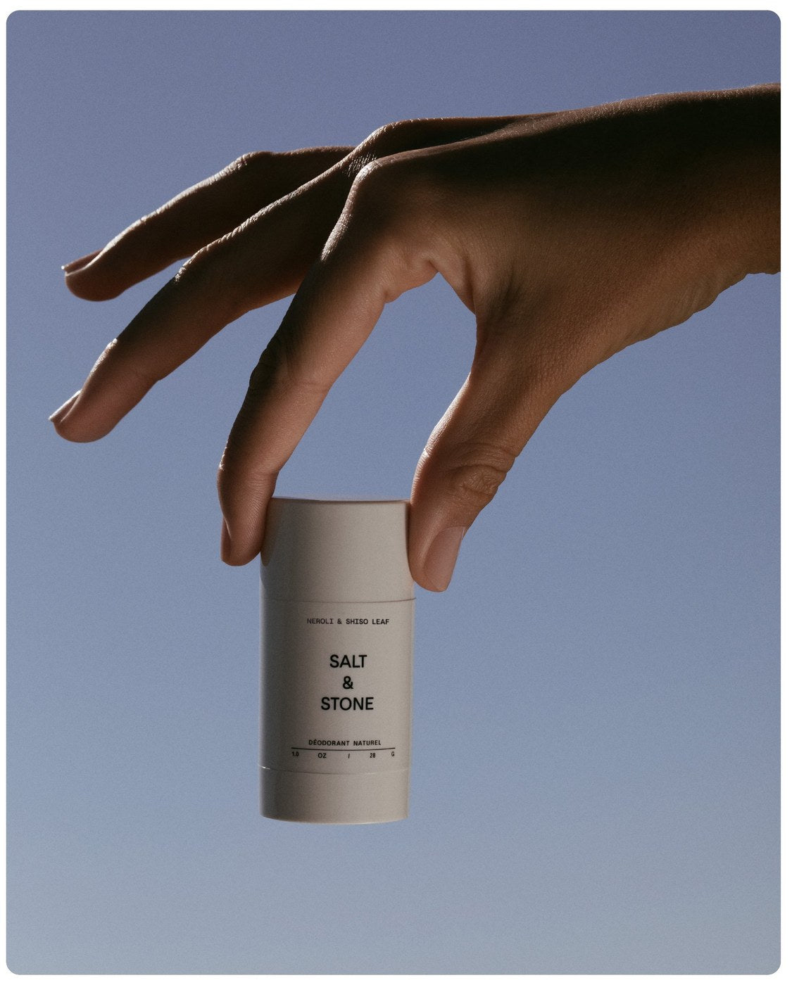 Salt & Stone Deodorant Neroli & Shiso Leaf in einer Hand — Lifestyle-Aufnahme vor blauem Himmel