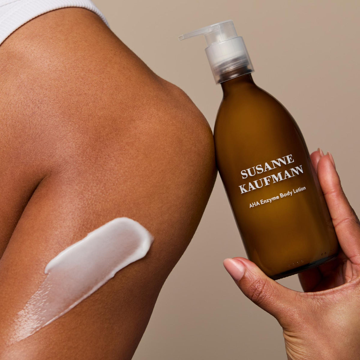 Susanne Kaufmann AHA Enzyme Body Lotion / AHA-Enzym-Körperlotion, 250ml – Lotion auf dem Arm, Flasche in der Hand