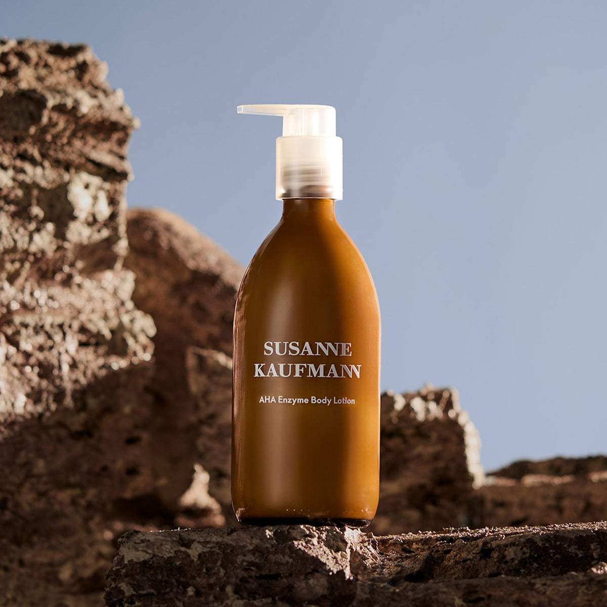 Susanne Kaufmann AHA Enzyme Body Lotion / AHA-Enzym-Körperlotion, 250ml – Flasche auf Felsen vor blauem Himmel