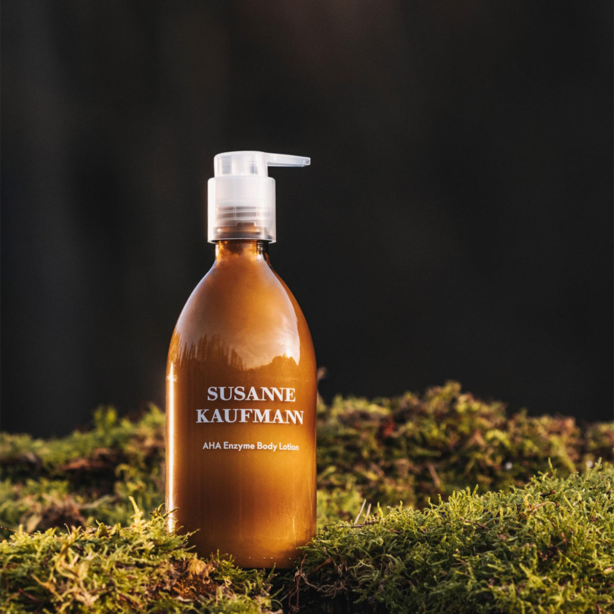 Susanne Kaufmann AHA Enzyme Body Lotion / AHA-Enzym-Körperlotion, 250ml – Flasche auf Moos im Abendlicht