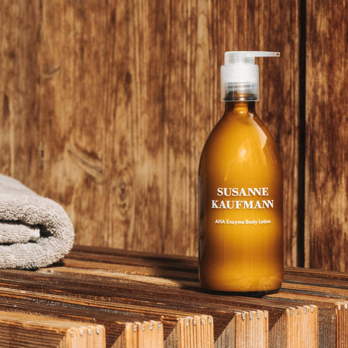 Susanne Kaufmann AHA Enzyme Body Lotion / AHA-Enzym-Körperlotion, 250ml – Flasche auf einer Holzbank