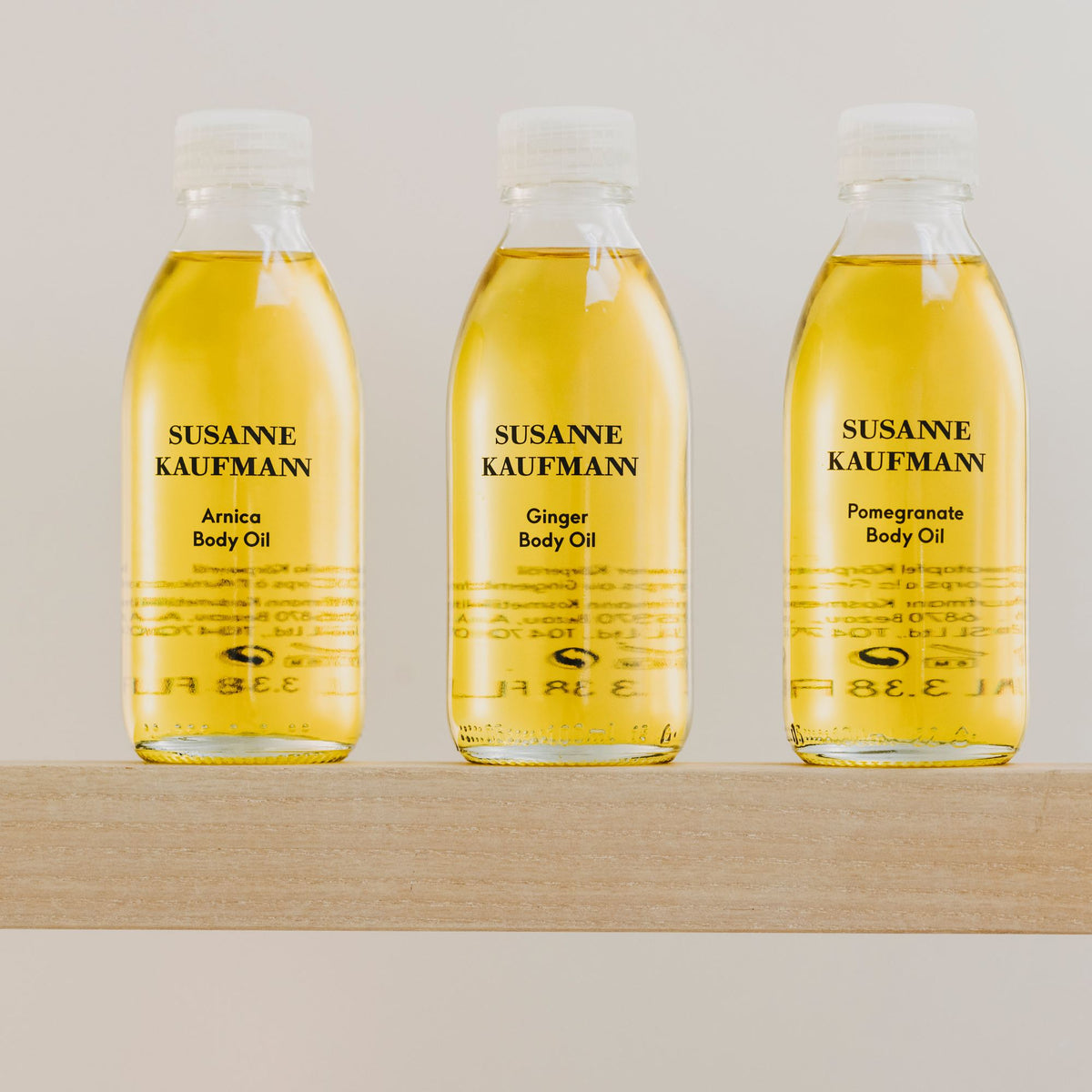 Susanne Kaufmann Arnica Body Oil / Arnika-Körperöl, 100ml – mit Ingwer- und Granatapfel-Körperöl auf einem Holzregal