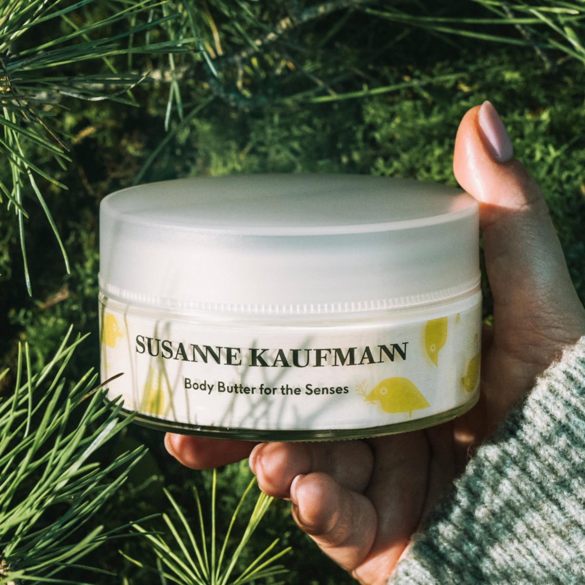 Susanne Kaufmann Body Butter for the Senses / Körperbutter, 200ml – Tiegel in der Hand zwischen Kiefernzweigen