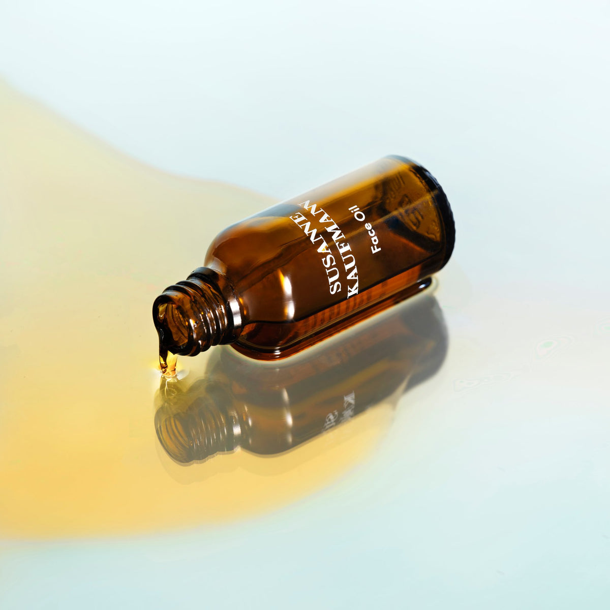 Susanne Kaufmann Face Oil / Gesichtsöl, 30ml – liegende Flasche mit ausgelaufenem Öl