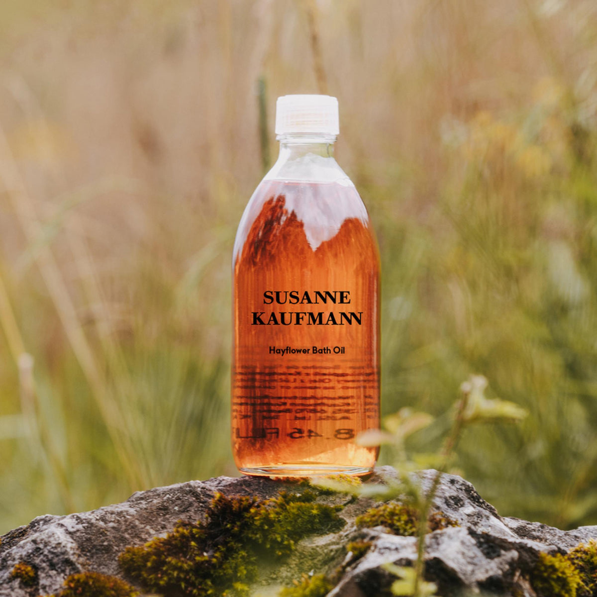 Susanne Kaufmann Hayflower Bath Oil / Heublumen-Ölbad, 250ml – Flasche auf einem bemoosten Stein in der Wiese